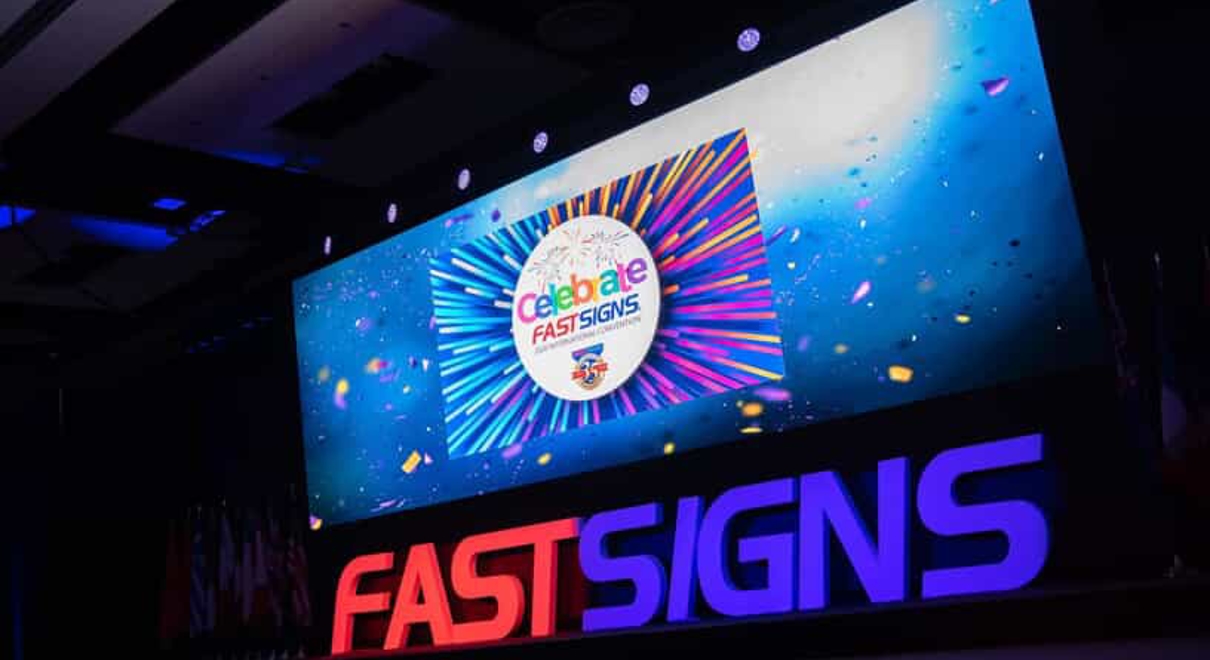 A screen advertises a FASTSIGNS celebration