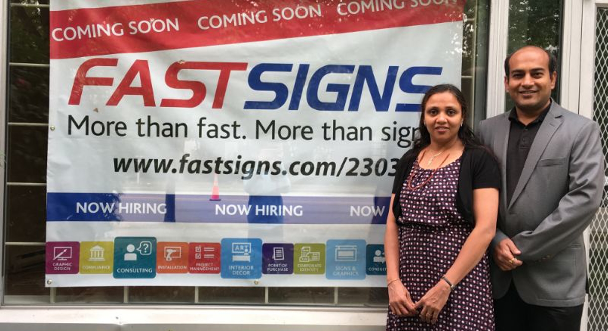 The Patels pose in front of their FASTSIGNS coming soon sign