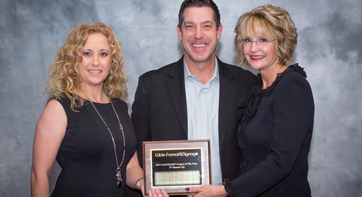 Owner Clint Ehlers (center) and account manager Angela Allison (left) received multiple recognitions at the 2018 FASTSIGNS Convention presented by Catherine Monson (right), CEO of FASTSIGNS International, Inc.
