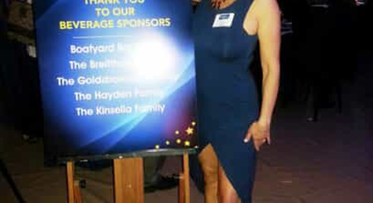 a woman poses next an event sign thanking sponsors