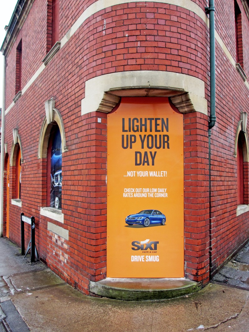 Sixt Lighten up Your Day Signage on Brick Wall Corner
