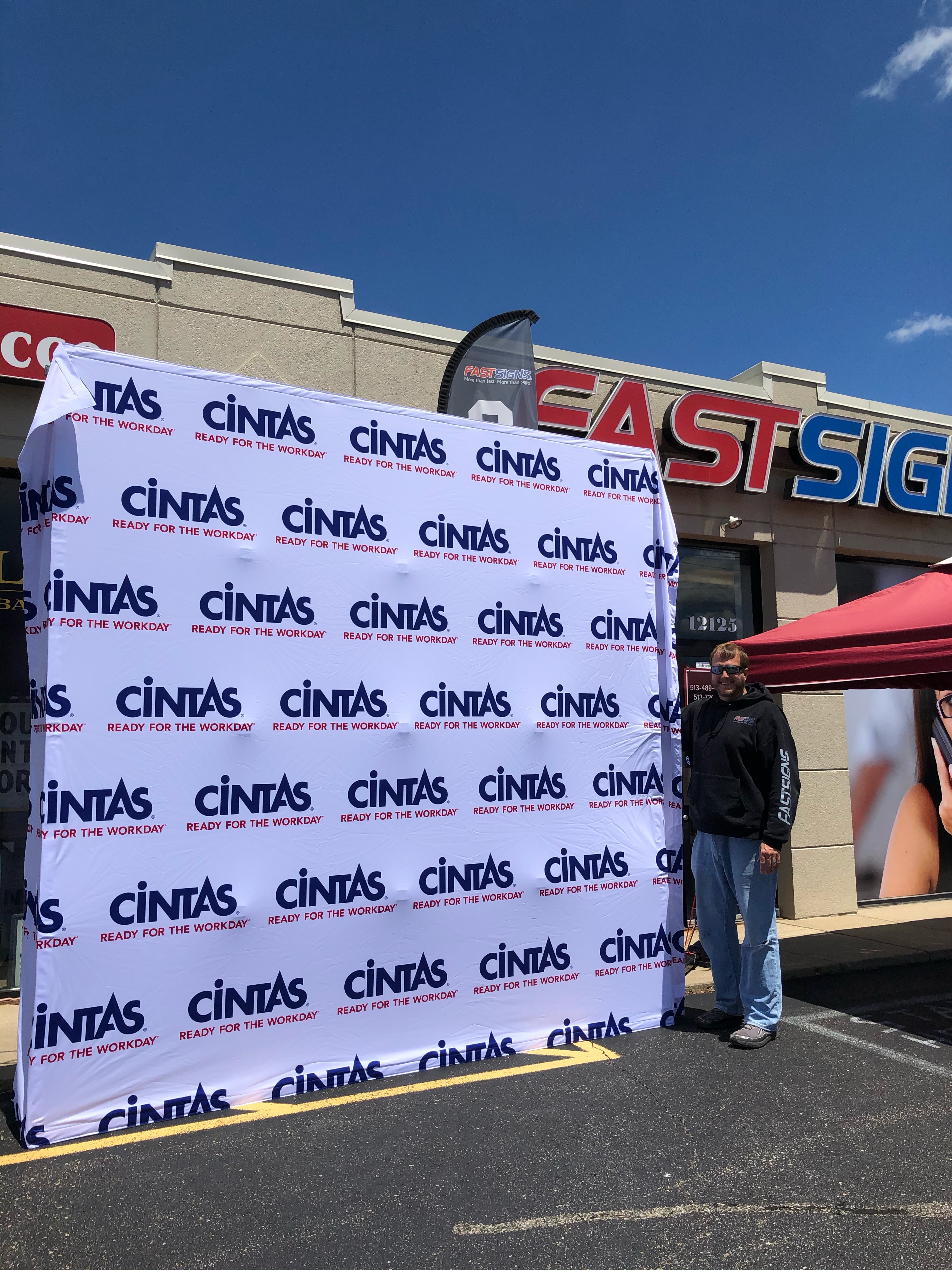 A man holding the white custom banner backdrop outside the fast sign office with canopy on the side