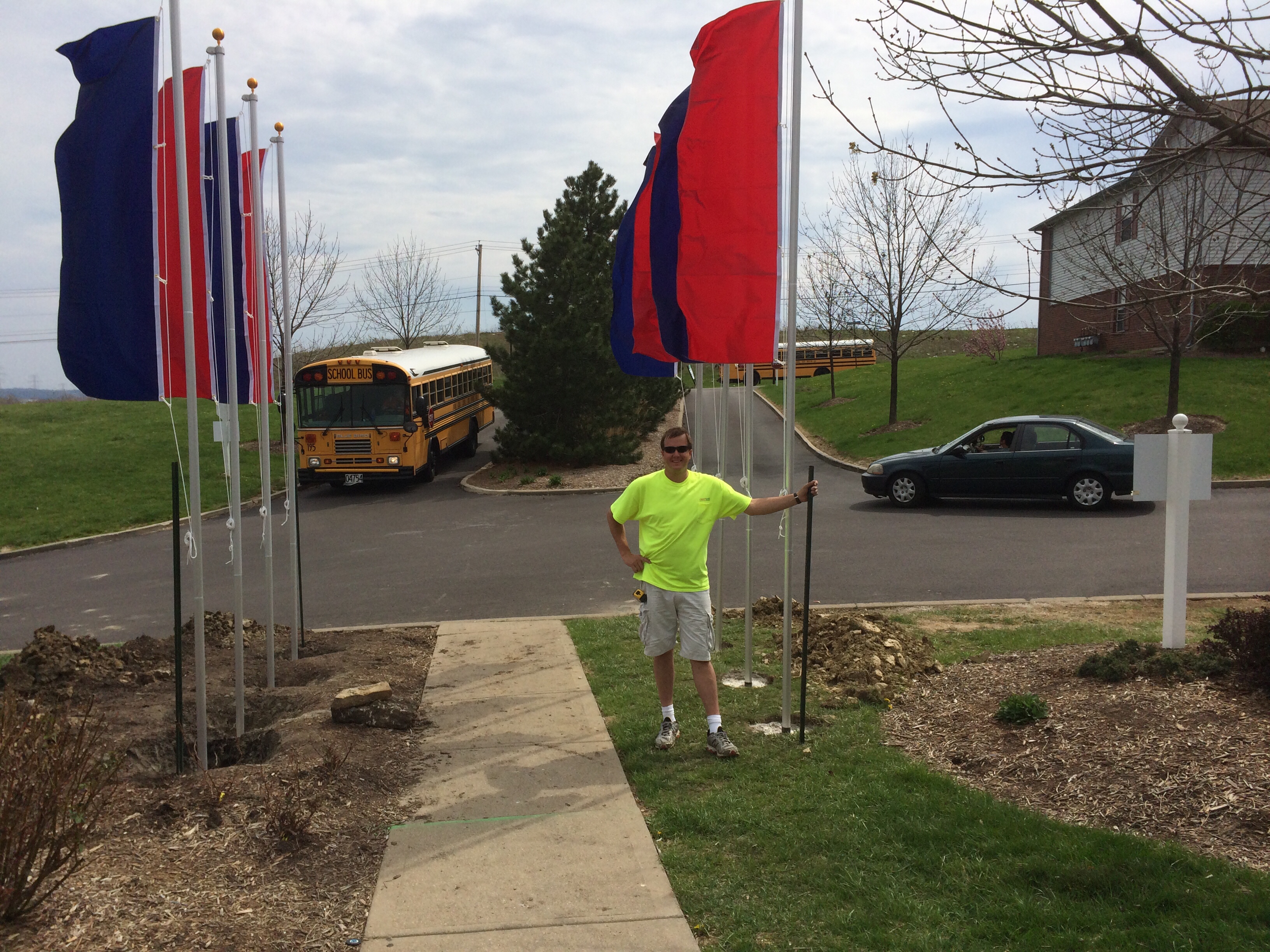 Man holding a flag pole with a school bus and a black car in the background