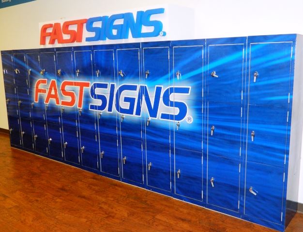 A FASTSIGNS sign hangs above lockers with the FASTSIGNS logo on them