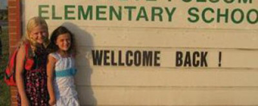 Two students pose next to a sign that says "wellcome back" with incorrect spelling