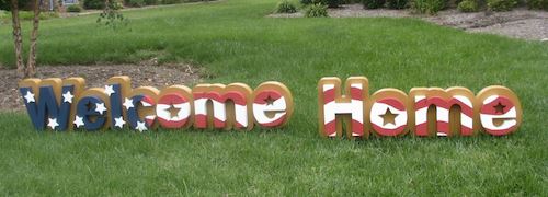 A patriotic dimensional lettering sign sits on the grass reading "Welcome Home"