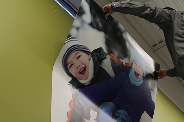 A wall graphic of children in the snow is being hung