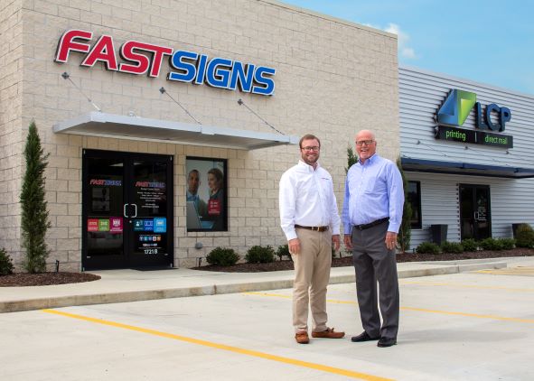 A father and son duo stand outside of a FASTSIGNS storefront