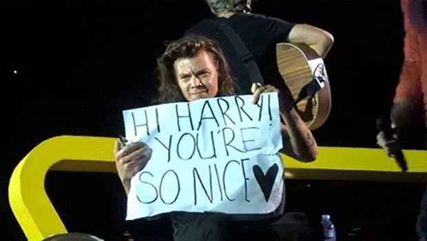 Harry Styles holds up a poster by a fan where he corrected the grammar written on it