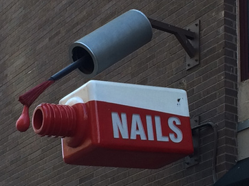 A nail salon has a giant bottle of nail polish outside of their shop