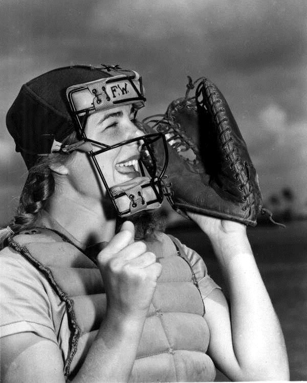 A black and white image of a female dressed to be a baseball catcher