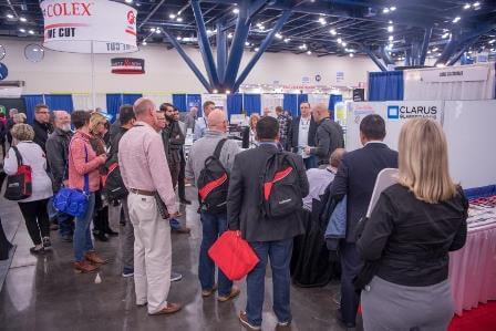 A crowd stands around a trade show booth to hear more information