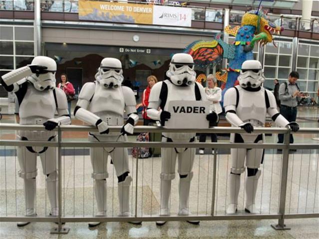 Four people dressed as storm troopers from Star Wars hold a sign that says "Vader"