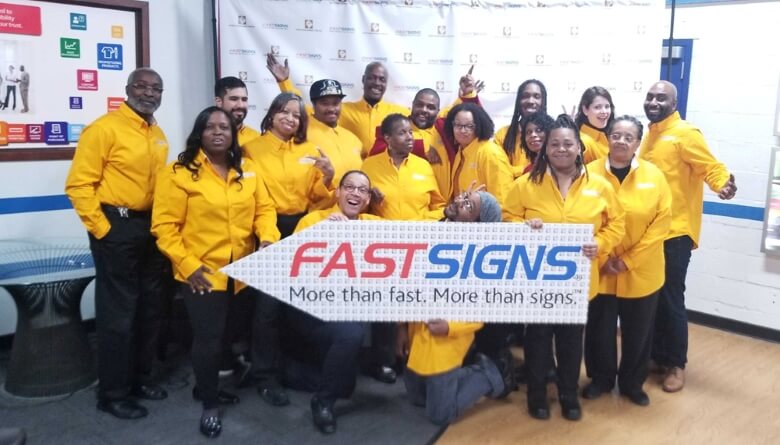 The employees of FASTSIGNS Washington DC pose together with a FASTSIGNS sign