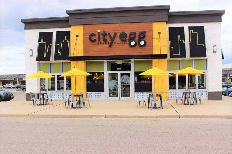 outside City Egg restaurant showing custom building sign, awnings, and yellow umbrellas