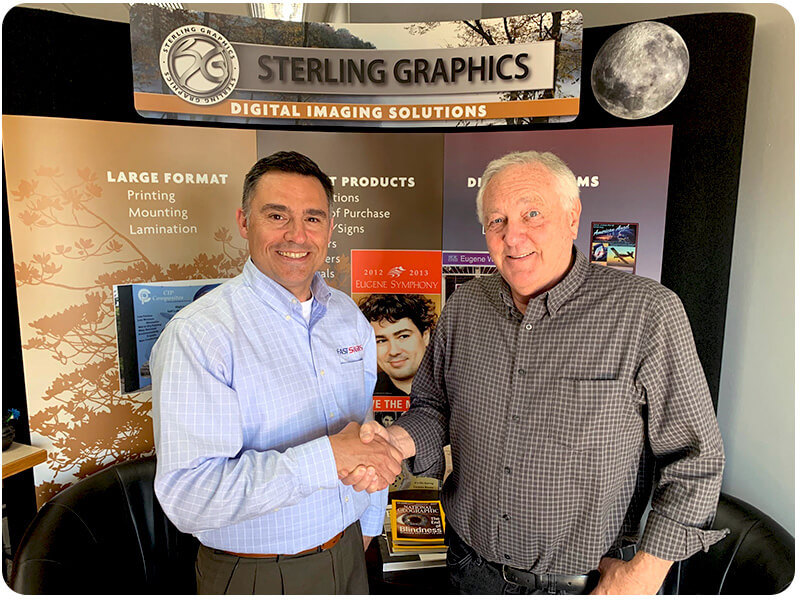two men shaking hands in front of Sterling Graphics display