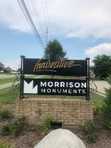 Morrison monument  on the side of the road with electric wires on top and plants on the side of the monument