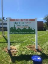 For sale signage of big hill commercial group on the lot with blue pale on the side and house on the back