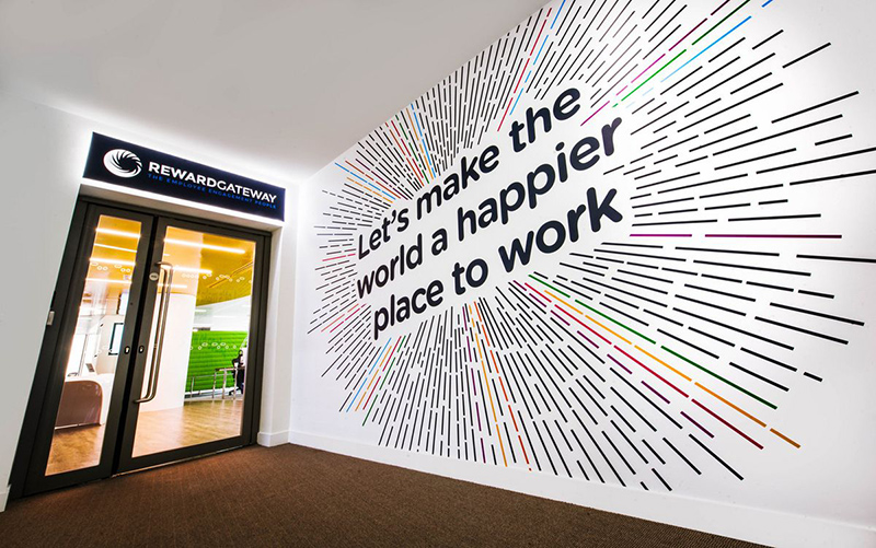 a wall graphic says "Let's make the world a happier place to work"