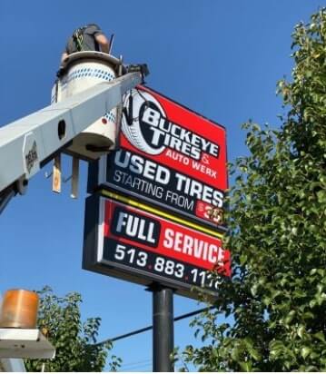 Crane truck carrying a man on top of buckeye tires signage 