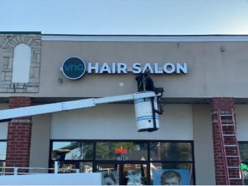 Crane truck carrying a man that's cleaning the VNG Hair salon signage 