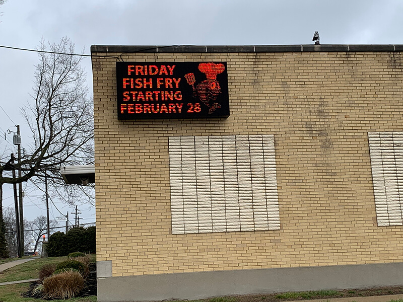 Black and red theme signage on the brick wall with wires, tree and pole