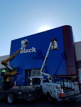 Two crane trucks on the building  fixing the building signage