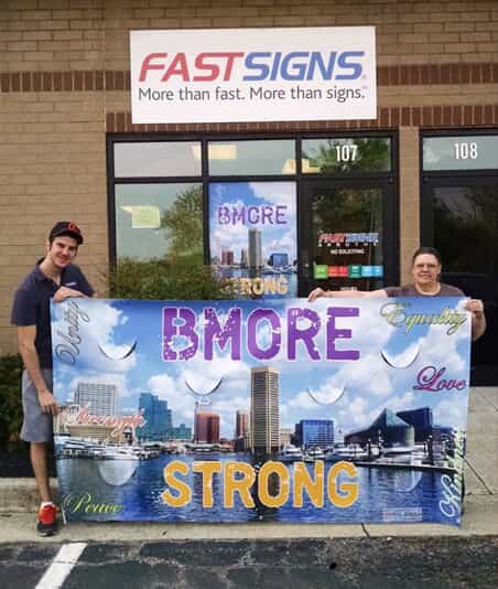 a Bmore Strong sign is held in front of a FASTSIGNS store