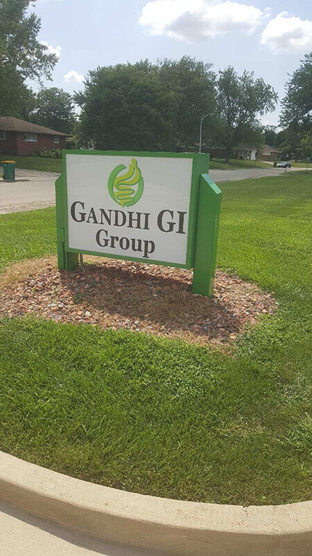 Gandhi Gi Signage on the side of the foot pathway with house and trees on the background