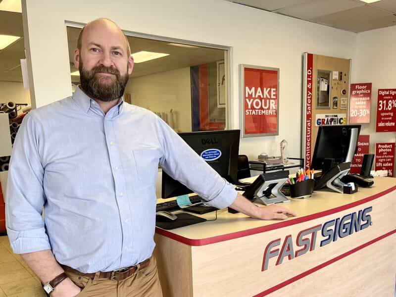 An image of Gregor next to the FASTSIGNS front desk in his lobby.