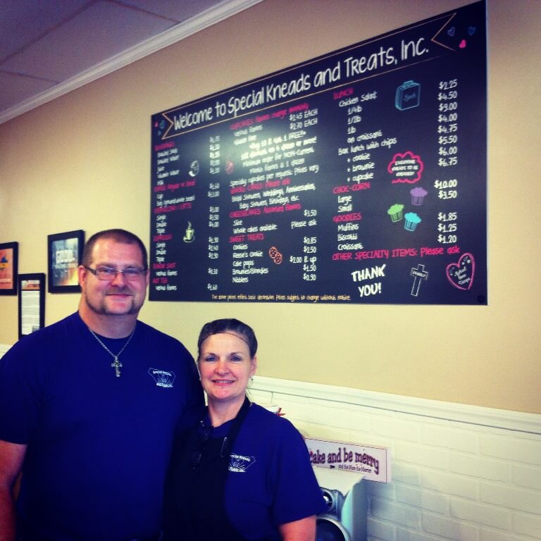 man and woman smiling standing in front of menu board