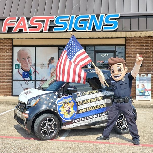 Patrol Stories mascot standing in front of wrapped vehicle at FASTSIGNS of Allen, TX