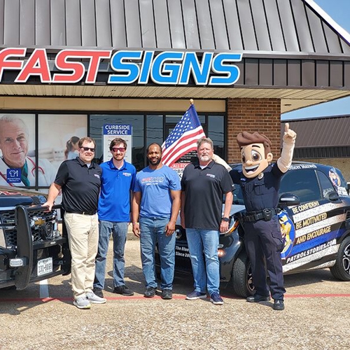 Patrol Stories mascot & group of men standing in front of wrapped vehicle at FASTSIGNS of Allen, TX