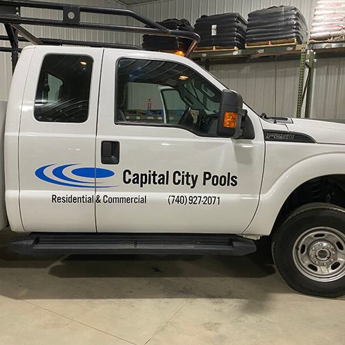 A white vehicle with letterings of capital city pools